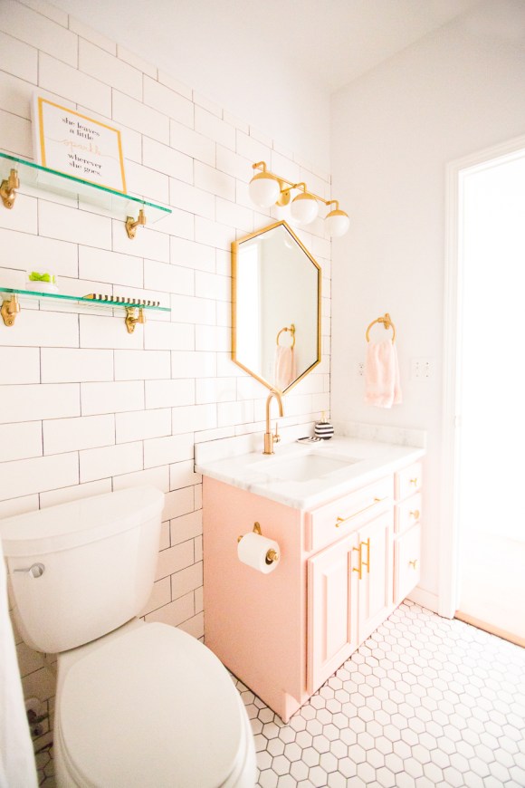 Modern-Glam-Blush-Girls-Bathroom-Design-gold-hexagon-mirror-blush-cabinets-gold-hardware-white-hexagon-floor-glass-shelves-pink-bathroom-cabinets-gold-orb-sconce-1-1