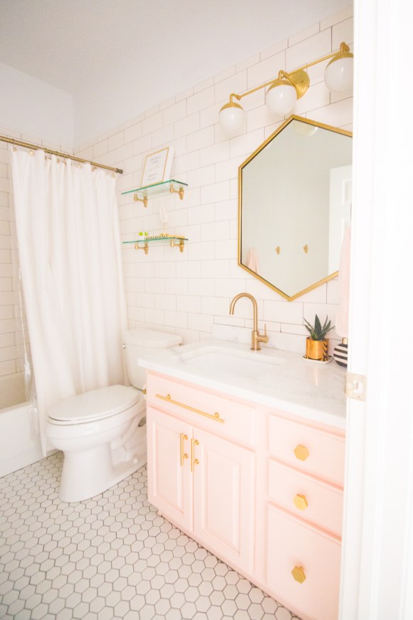 Modern-Glam-Blush-Girls-Bathroom-Design-gold-hexagon-mirror-blush-cabinets-gold-hardware-white-hexagon-floor-glass-shelves-pink-bathroom-cabinets-gold-orb-sconce-3-2